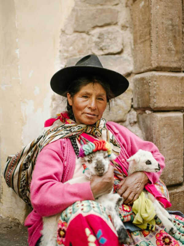 A woman in vibrant traditional clothing holds two goats in a rustic Peruvian setting. indigenous nutrition