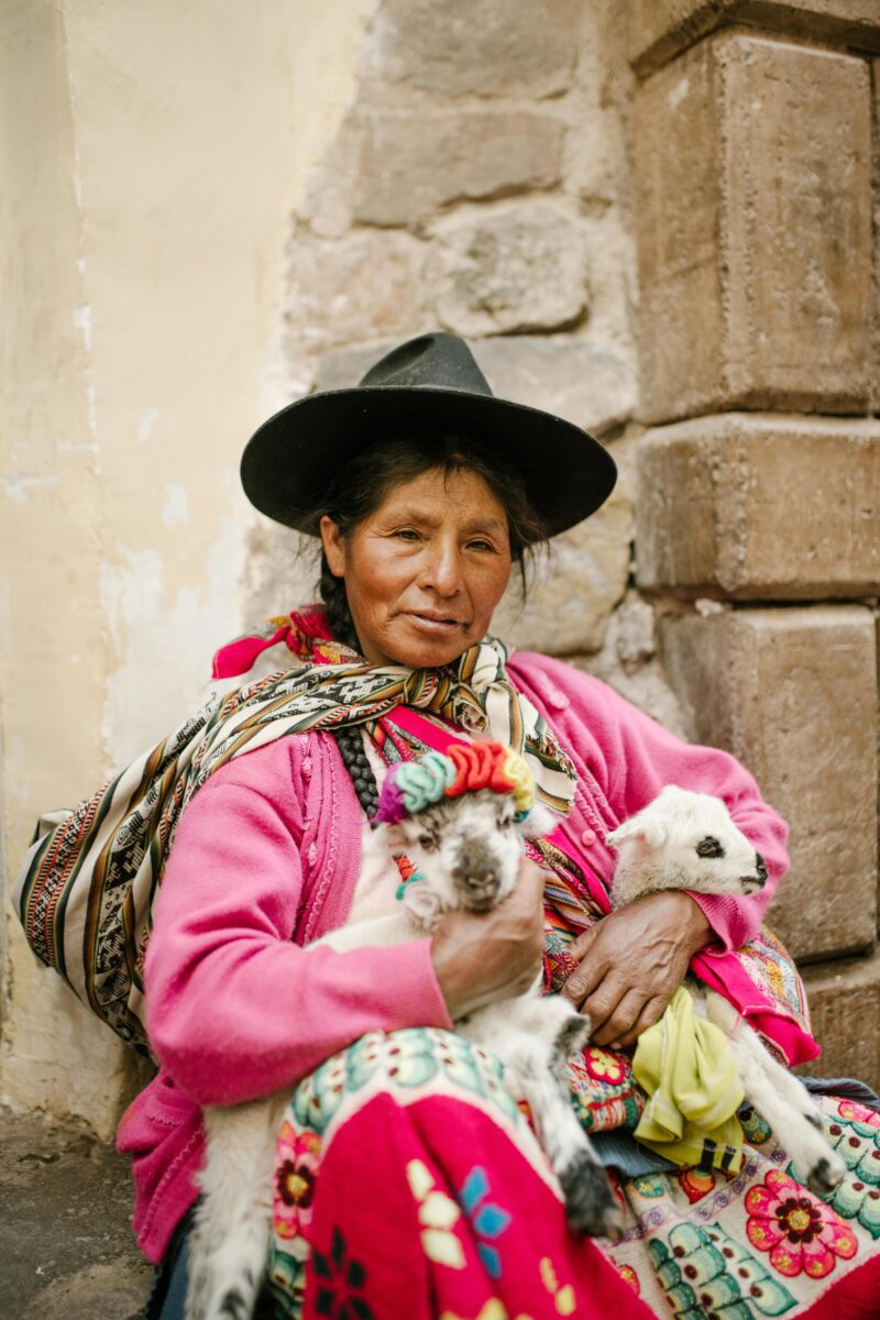 A woman in vibrant traditional clothing holds two goats in a rustic Peruvian setting. indigenous nutrition