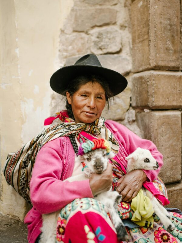 A woman in vibrant traditional clothing holds two goats in a rustic Peruvian setting. indigenous nutrition and physical degeneration
