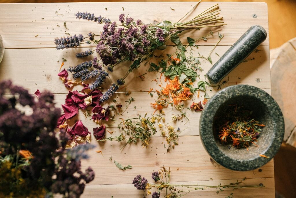 Flat lay of dried herbs and flowers with a stone mortar and pestle on a rustic wooden table. Mountain rose herbs.