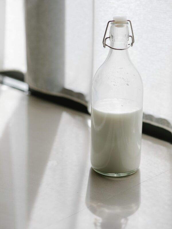 A milk bottles filled with fresh milk placed on a sunlit floor indoors.