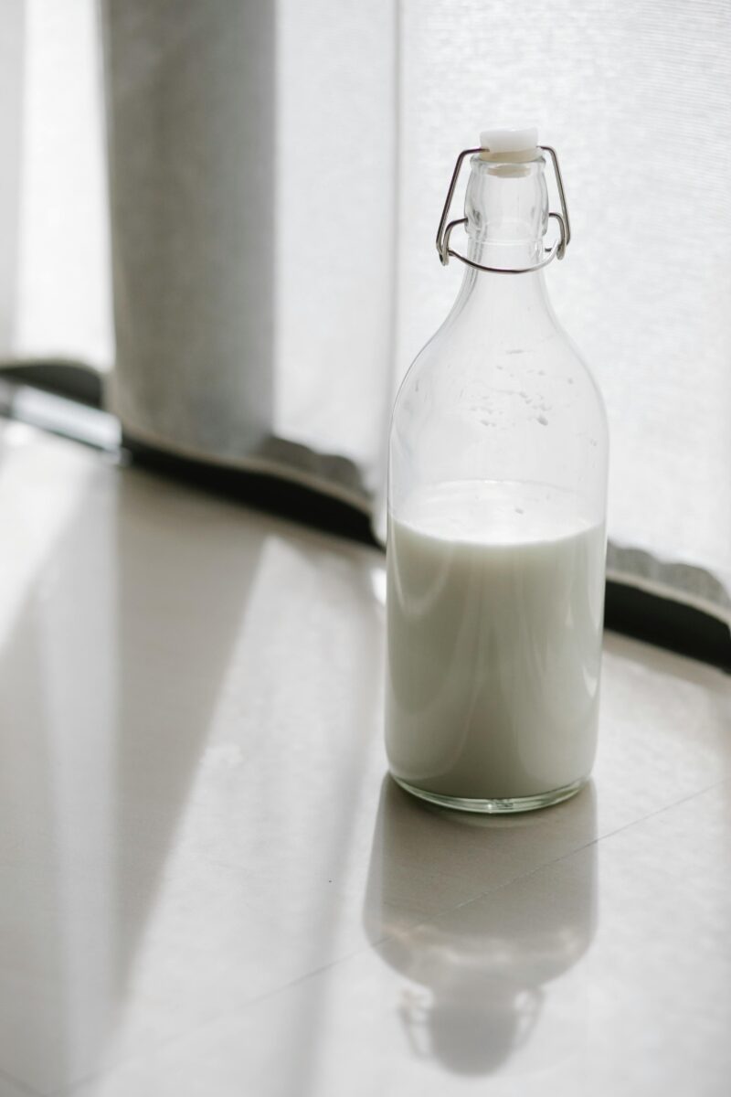 A milk bottles filled with fresh milk placed on a sunlit floor indoors.