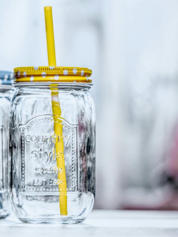 Close-up of two glass jars with polka dot lids and straws, offering a rustic aesthetic, glass mason jar