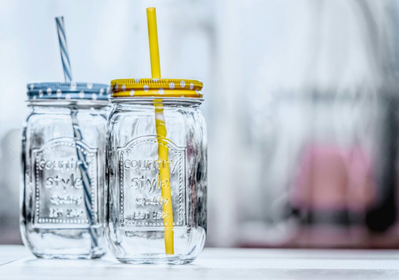 Close-up of two glass jars with polka dot lids and straws, offering a rustic aesthetic, glass mason jar