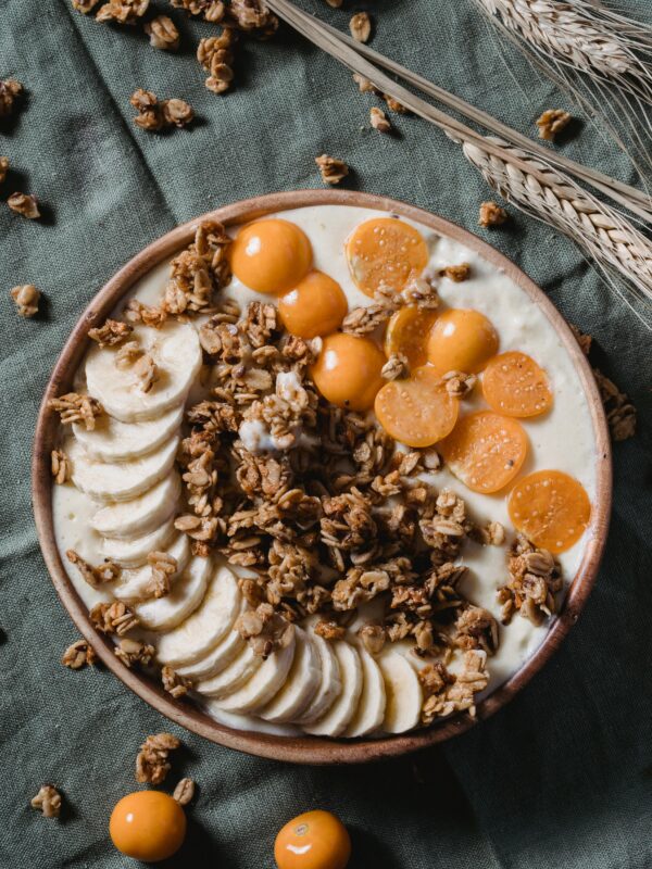 Top view of a healthy breakfast bowl with banana slices, granola, and golden berries on a rustic fabric backdrop. nourishing traditions