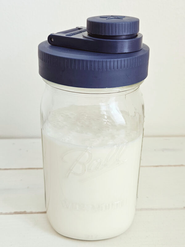Milk kefir in a glass mason jar with a blue easy pour spout wide mouth mason jar lids which is made in the USA. Glass mason jar is sitting on a table.