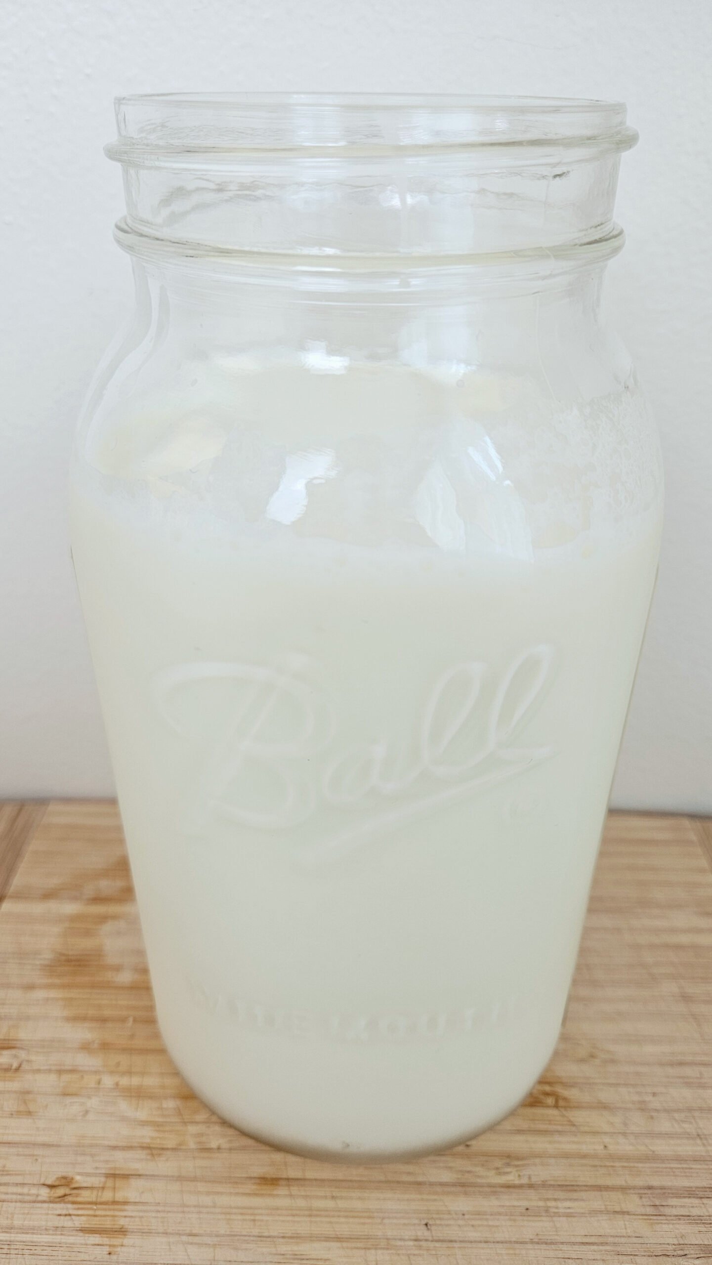 Half gallon jar of raw milk sitting on top of a wooden cutting board.