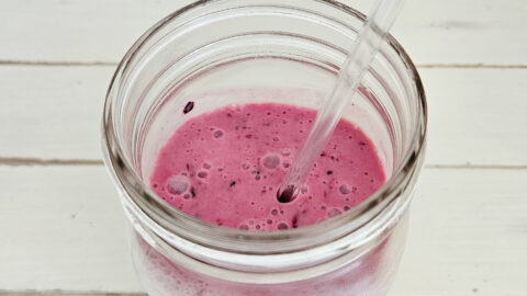 Top View of mixed berry milk kefir smoothie in a quart size mason jars. Glass straw sticking out of the jar. Smoothie is a rich magenta color with bubbles present on top.