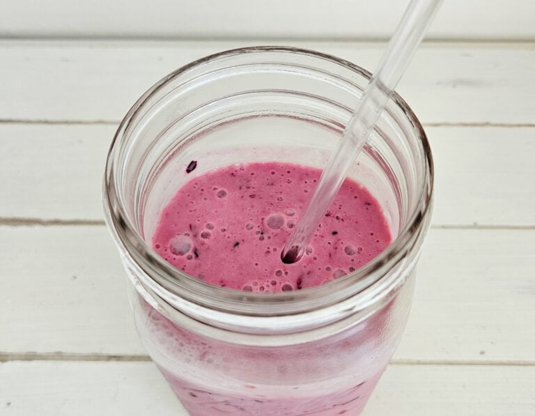 Top View of mixed berry milk kefir smoothie in a quart size mason jars. Glass straw sticking out of the jar. Smoothie is a rich magenta color with bubbles present on top.