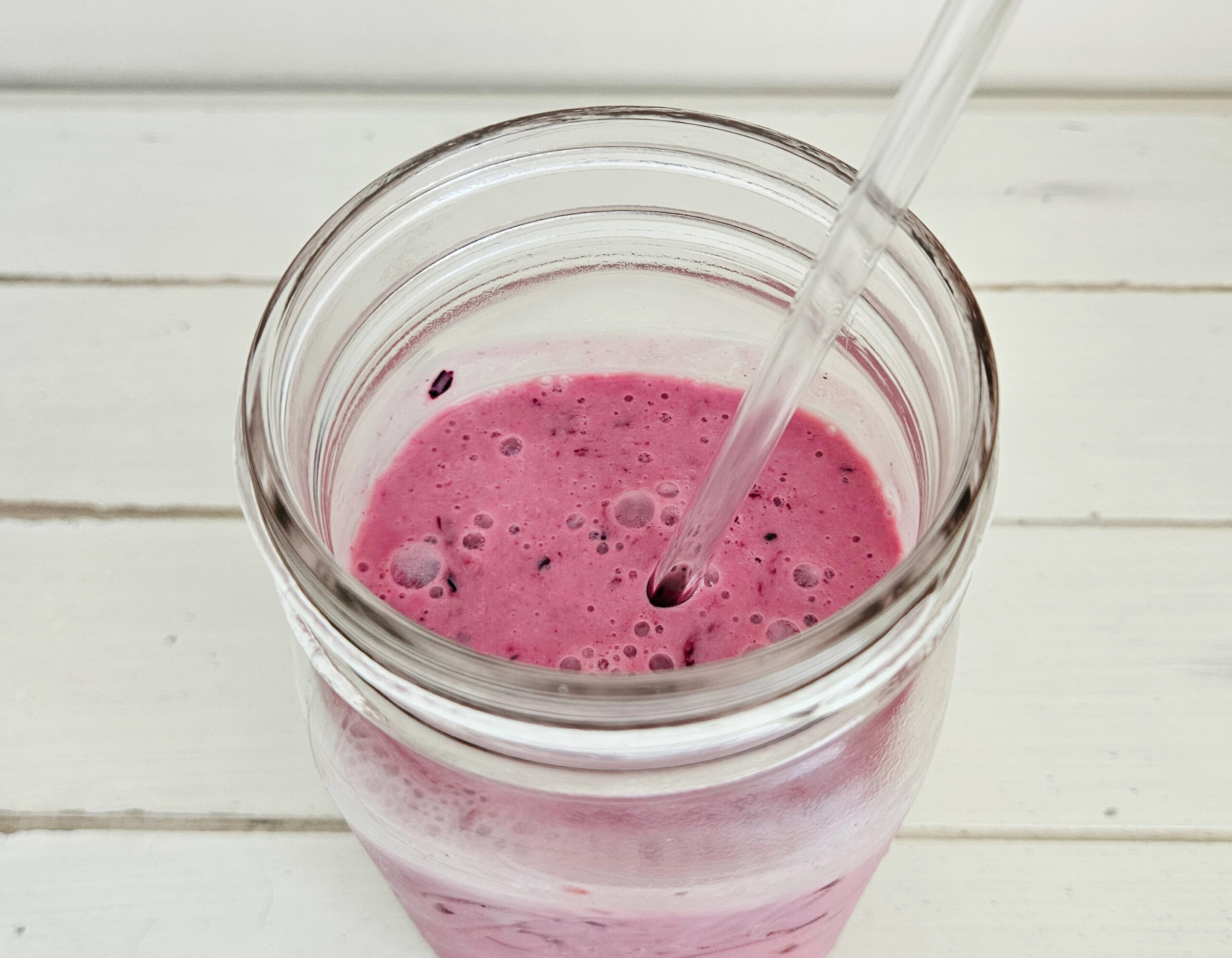 Top View of mixed berry milk kefir smoothie in a quart size mason jars. Glass straw sticking out of the jar. Smoothie is a rich magenta color with bubbles present on top.