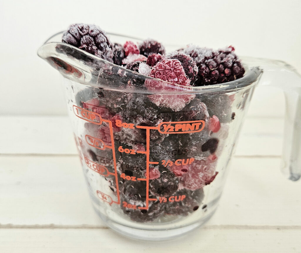 1 cup glass measuring cup filled with frozen mixed berries.