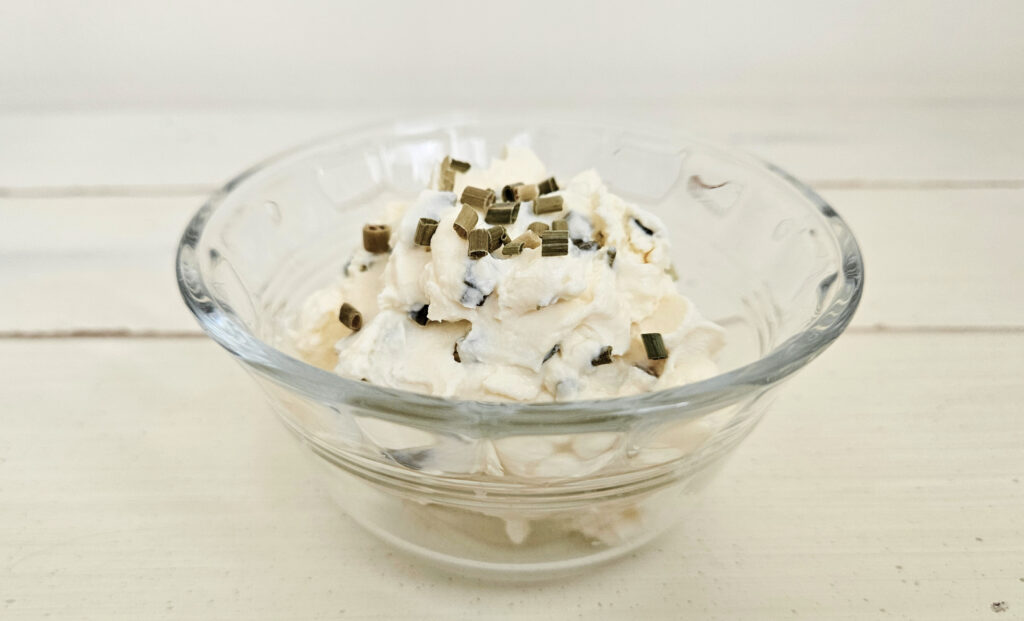 Glass bowl filled with white milk kefir cheese with green chives mixed in and sitting on top.