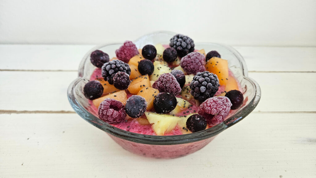 Kefir smoothie in a glass bowl with scalloped edges. Topped with cantaloupe, pineapple, blackberries, raspberries, blueberries, and chia seeds.