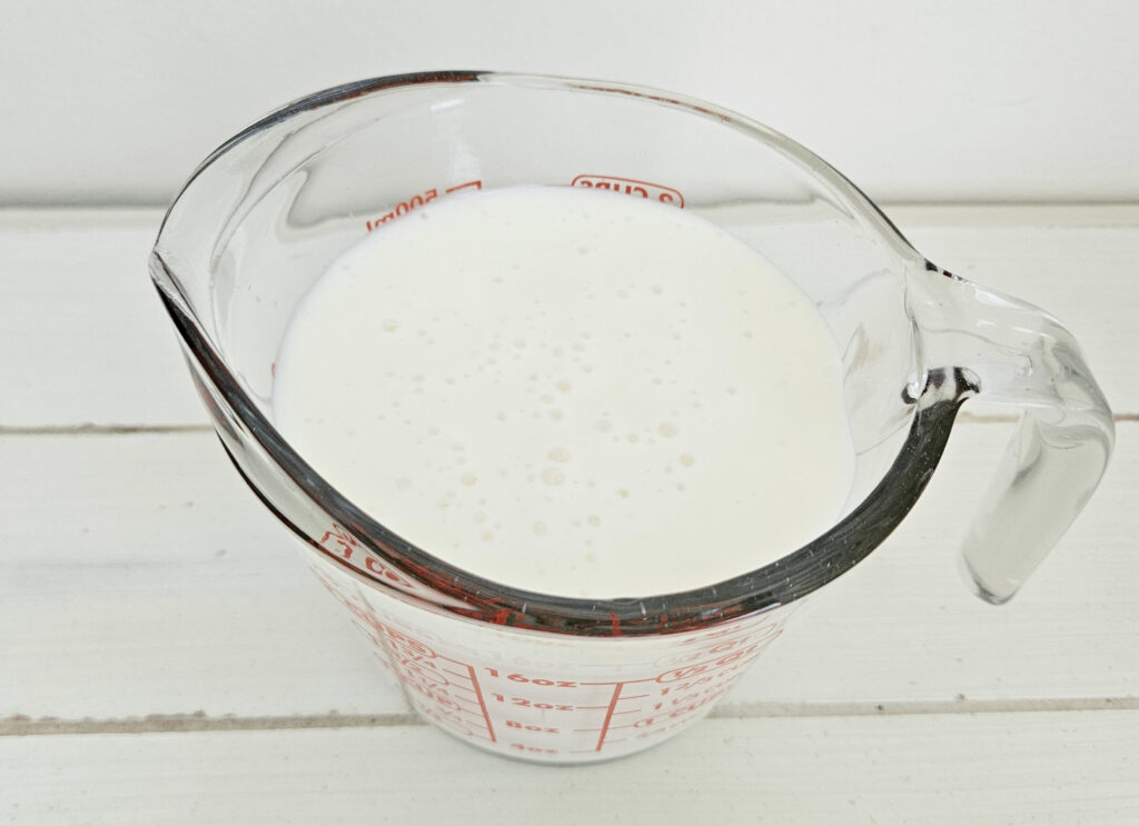 Milk kefir in a 2 cup glass measuring cup. White bubbles on top of kefir.
