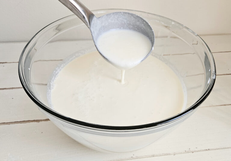 Large glass bowl filled with milk kefir. Metal ladle spooning kefir out of the bowl.