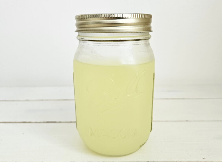 Pint size mason jar filled with yellow way. Gold mason jar lid. Sitting on cream colored table.