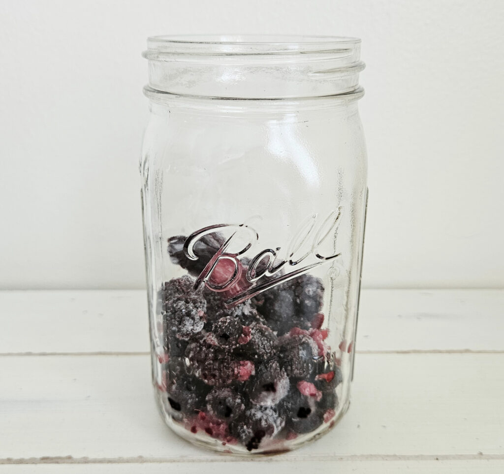 Quart size glass mason jar filled with heaping cup of frozen mixed berries. Berries are purple and red.