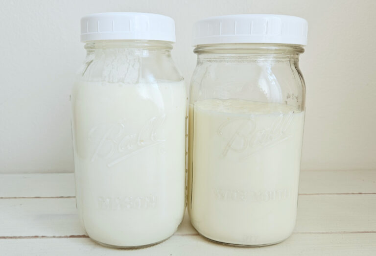 Two mason jars filled with milk kefir sitting on top of a table. White plastic lids on both jars.