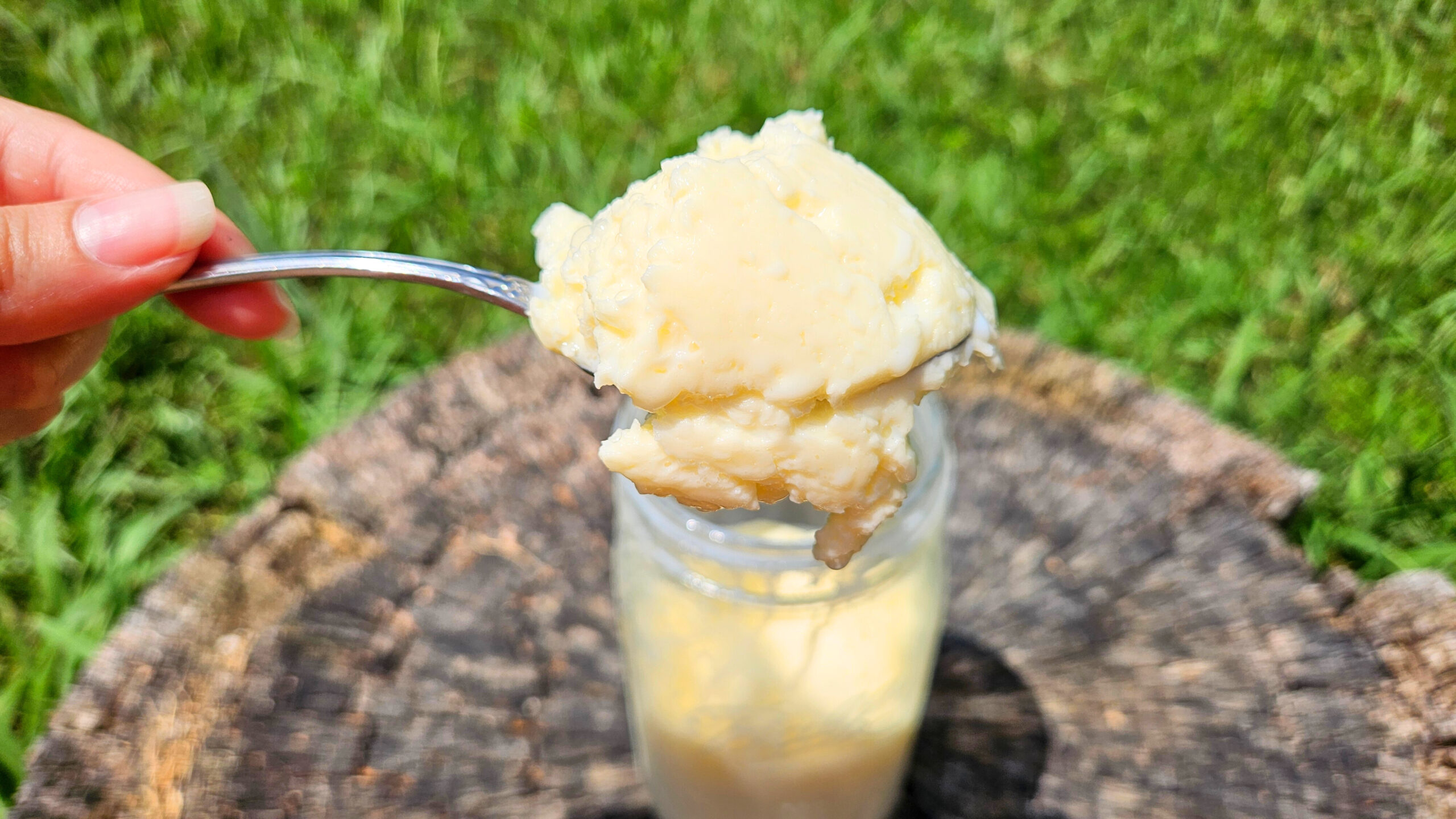 Homemade butter on a stainless steel spoon. Wide mouth mason jar with butter and buttermilk blurry in the background.