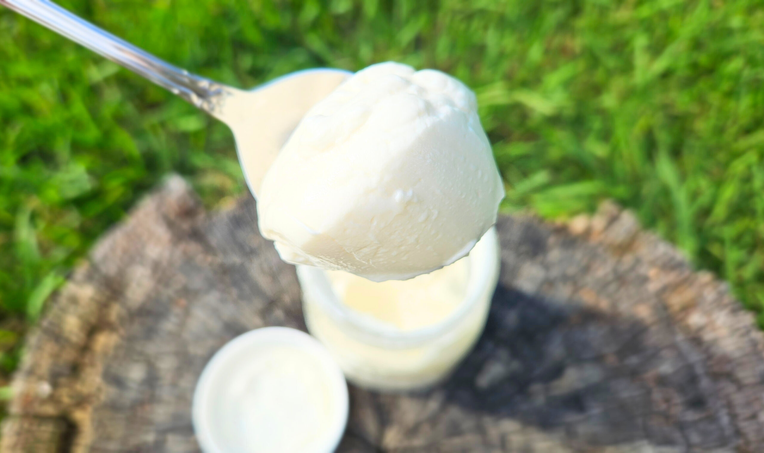 Homemade whipped cream on top of a spoon. Mason jar full of whipped cream and a white lid blurry in the background.