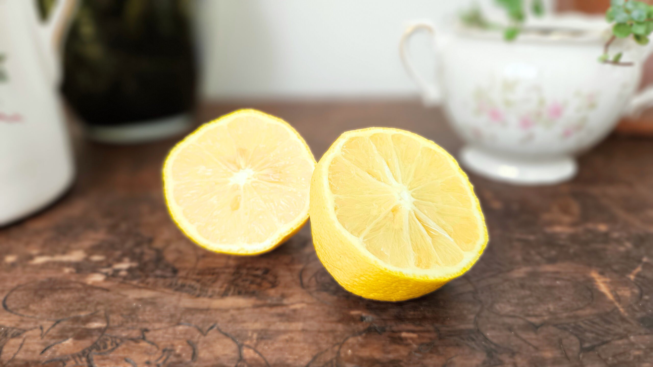 A bright yellow lemon sliced in half. Sitting on top of a brown wooden trunk with plants in the background.