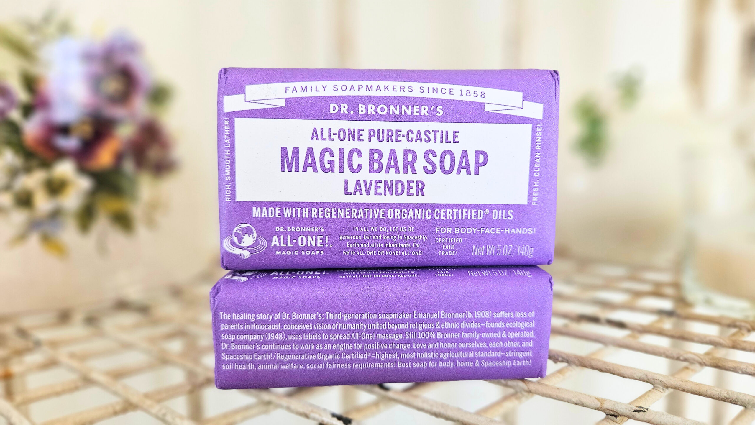 2 bars of Dr. Bronner's lavender castile soap stacked on top of each other. Sitting on a metal wire rack with pottery in the background.