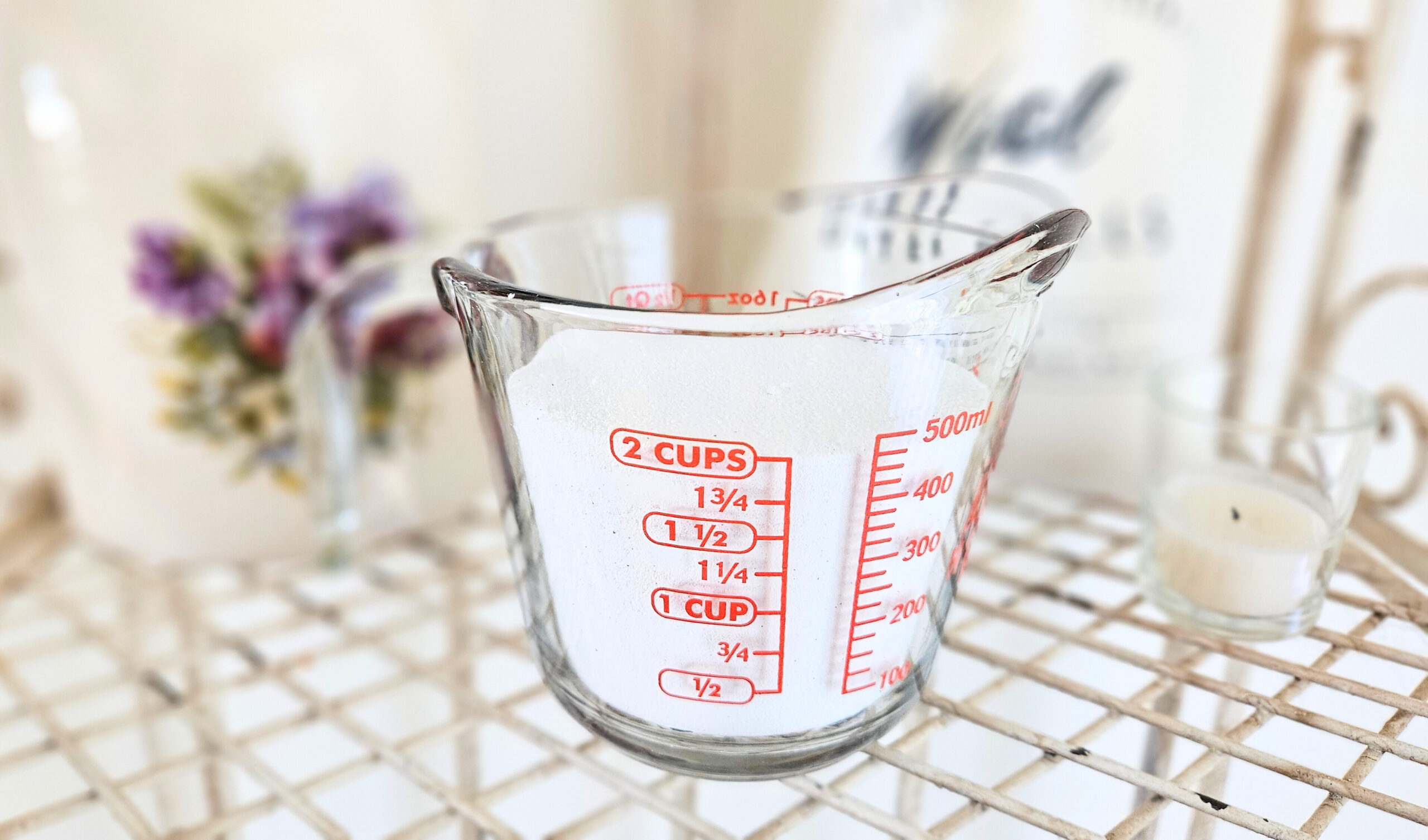 A glass measuring cup filled with two cups of borax. Borax is a white powdery mixture.