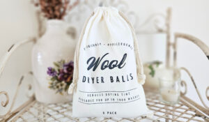 A cloth bag filled with wool dryer balls. The bag has "wool dry balls" written on the front in a dark navy color.