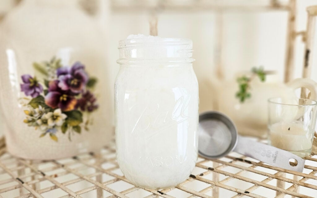 Pint jar of thick white liquid laundry detergent with a quarter cup stainless steel measuring cup.