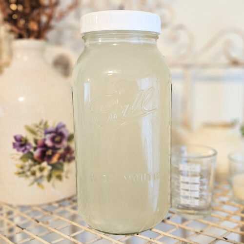 Half gallon mason jar filled with light yellow homemade liquid laundry detergent.