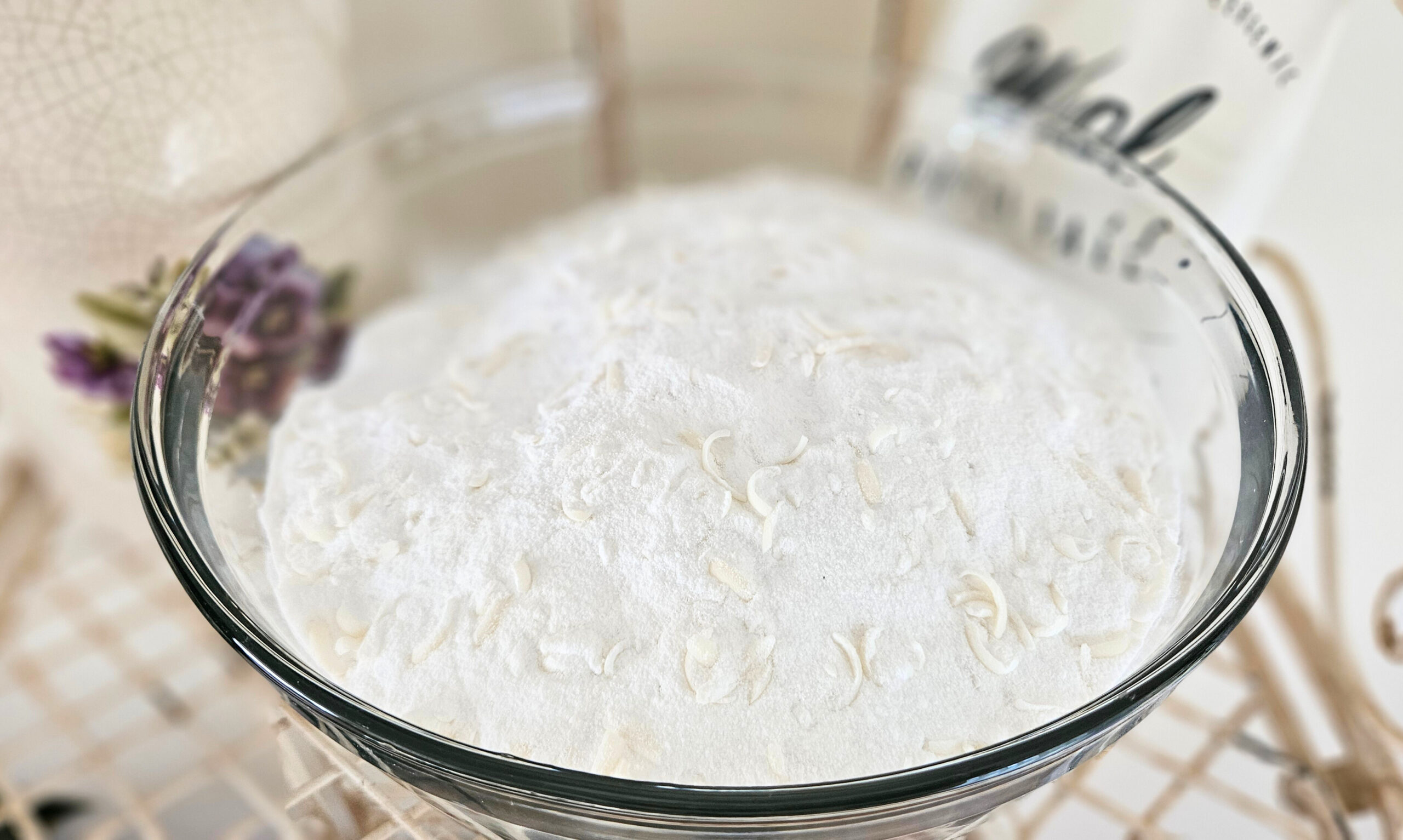 A glass bowl filled with white and cream colored powder laundry detergent.