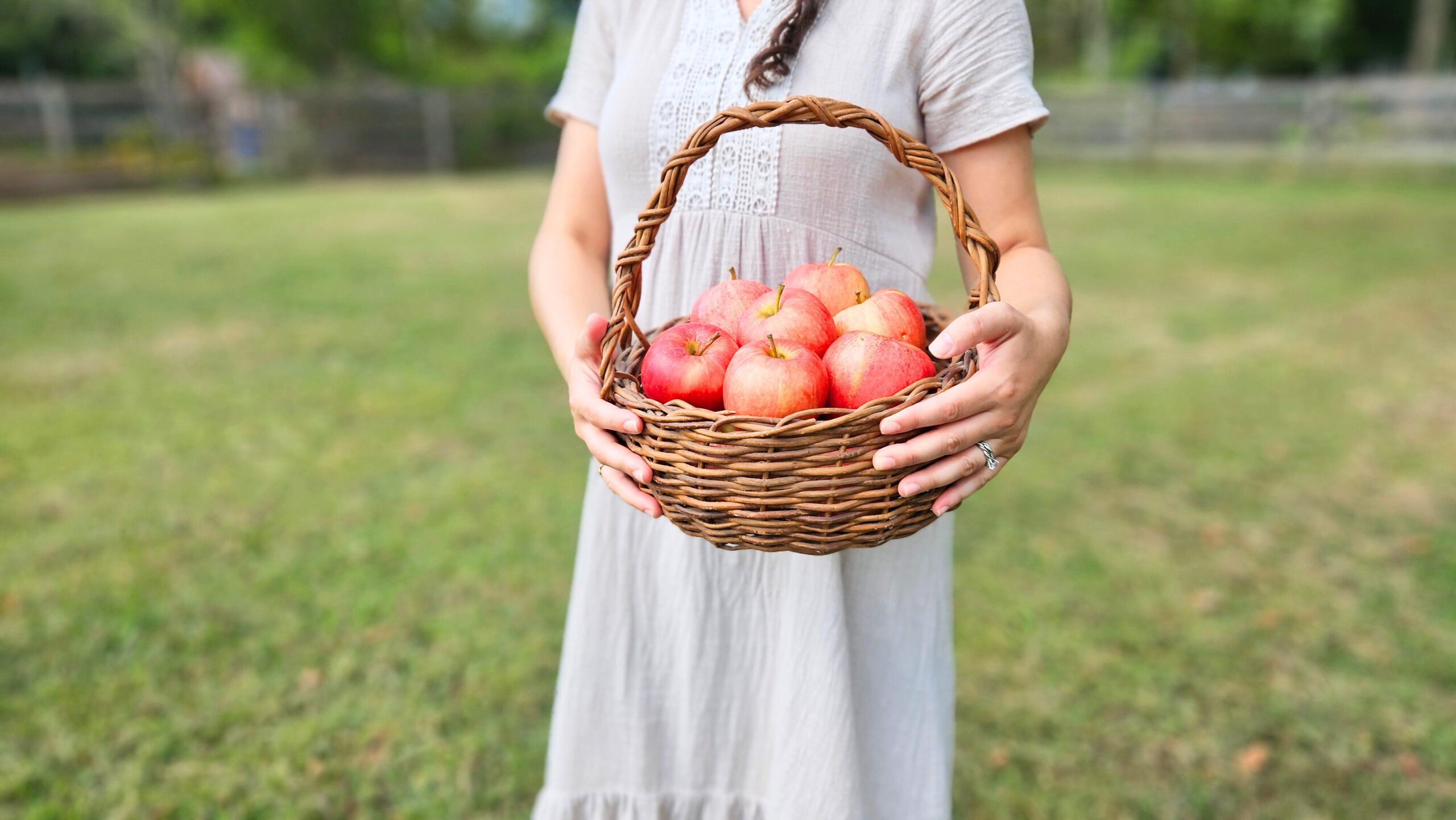 A woman outside holding a basket of red apples.