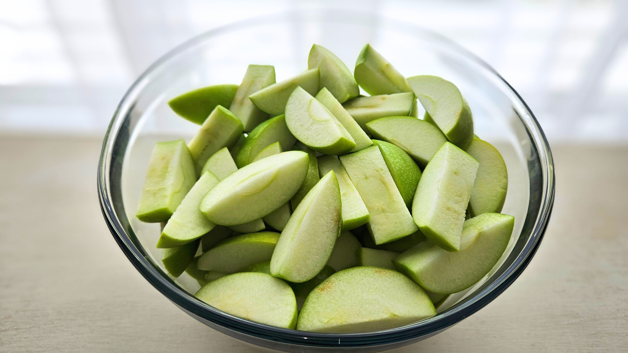A glass bowl filled with sliced grannysmith apples.