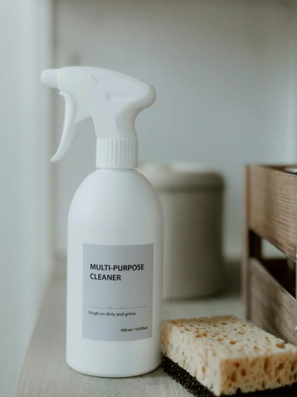 A spray bottle of aunt fannie's all-purpose cleaner with sponge on a bathroom shelf.