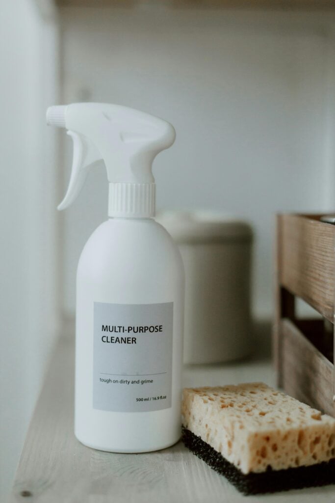 A spray bottle of aunt fannie's all-purpose cleaner with sponge on a bathroom shelf.