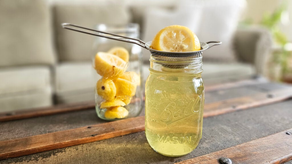 Quart size mason jar filled with lemons. Pint size mason jar filled with lemon vinegar concentrate. Fine mesh strainer with a lemon scrap on top.