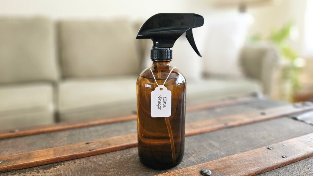Amber glass spray bottle filled with citrus vinegar cleaning spray. Spray bottle is labeled.