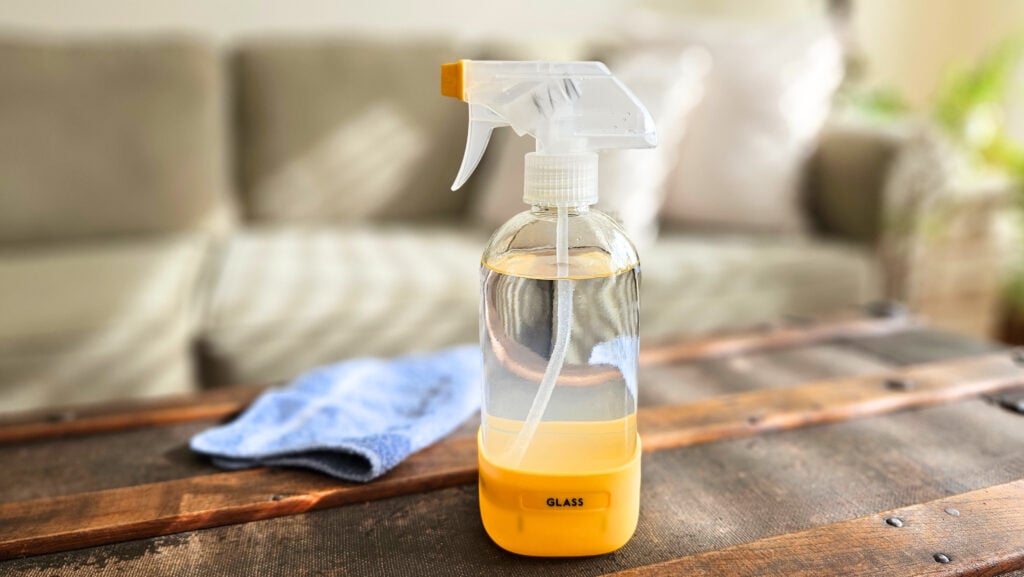 Clear glass spray bottle of homemade glass and window cleaner with a blue cleaning cloth next to it.
