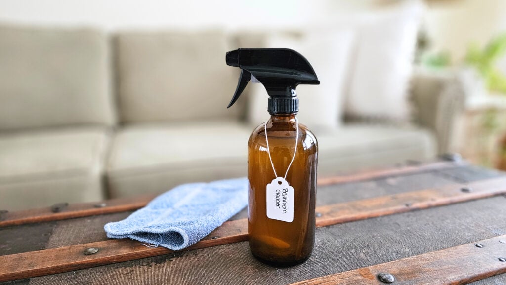 Bottle of DIY bathroom cleaner and a blue cleaning cloth.