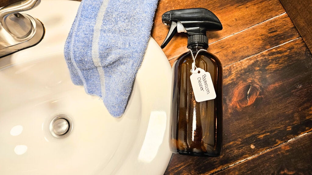 Amber glass spray bottle of bathroom cleaner laying on bathroom countertop next to sink.