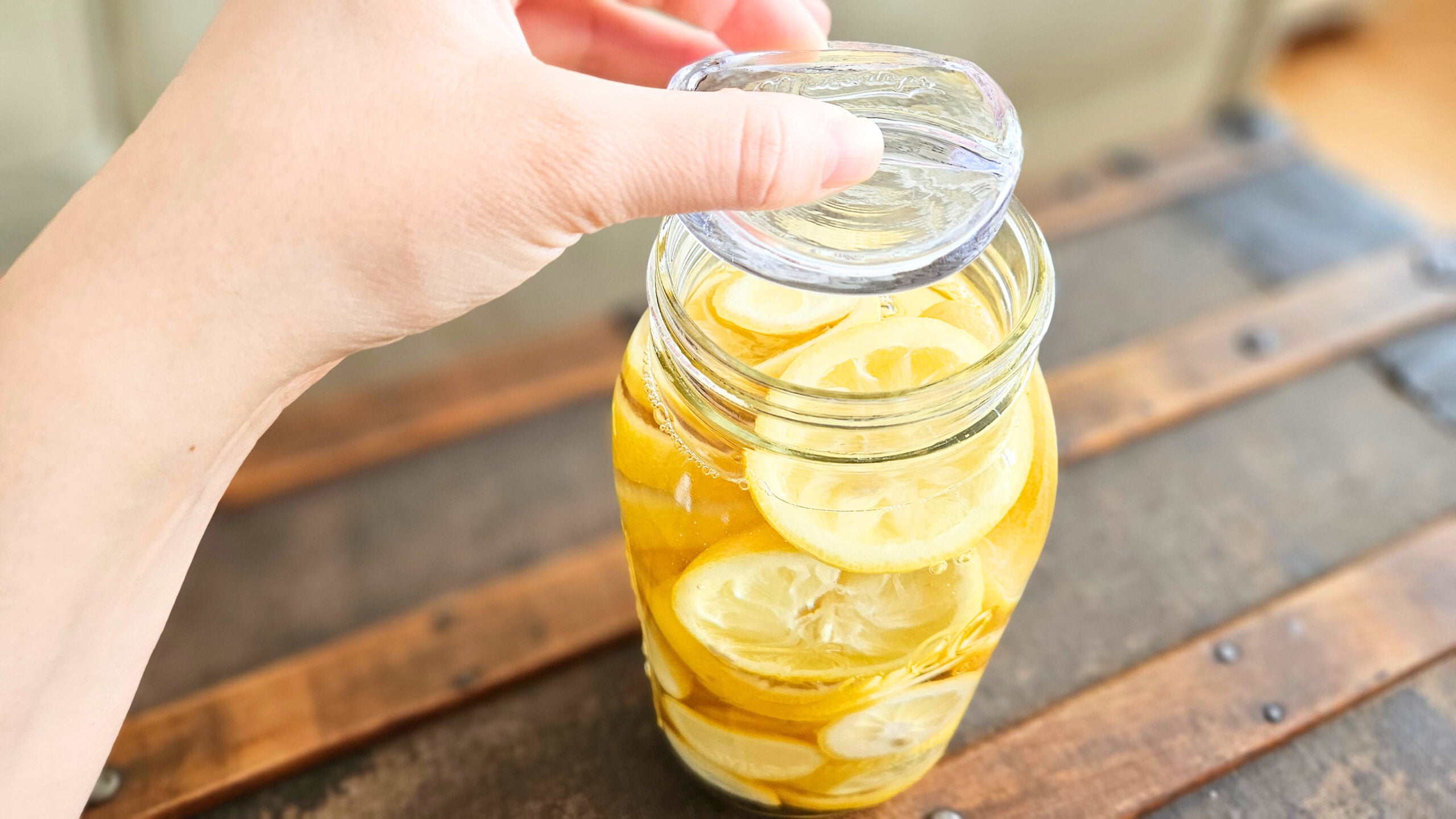 Adding a glass fermentation weight on top of lemon rinds in a jar filled with distilled white vinegar.