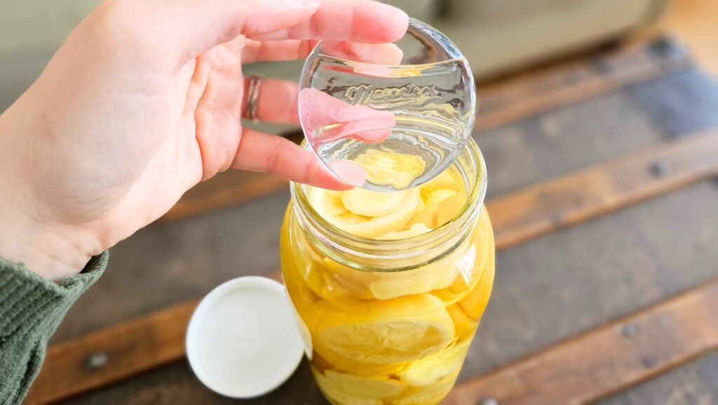 Holding a glass fermentation weight above a mason jar filled with lemons and vinegar.