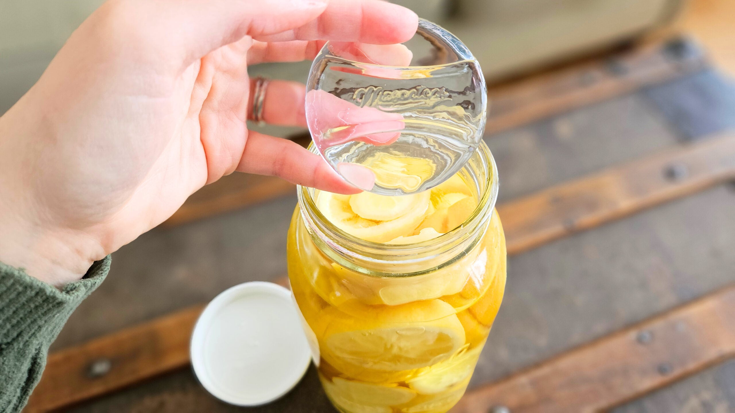 Holding a glass fermentation weight above a mason jar filled with lemons and vinegar.