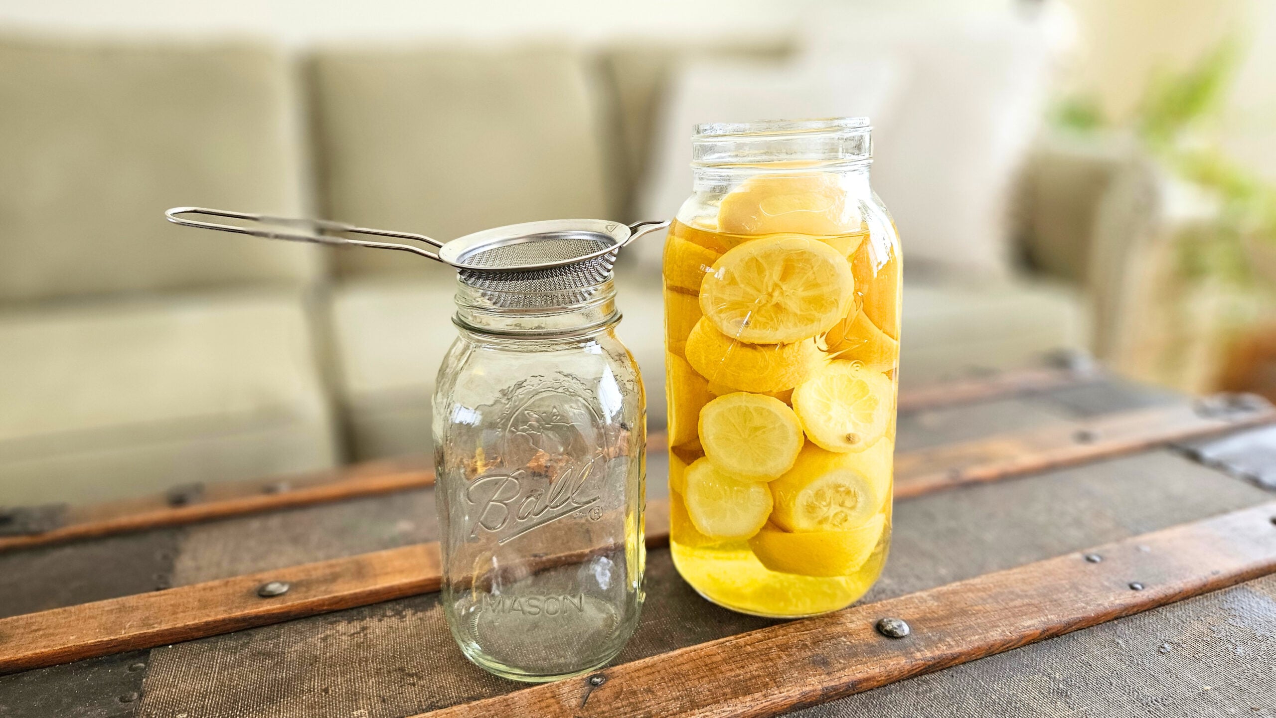 Half gallon mason jar of lemons and distilled white vinegar, an empty quart size mason jar, and 1 fine mesh strainer.