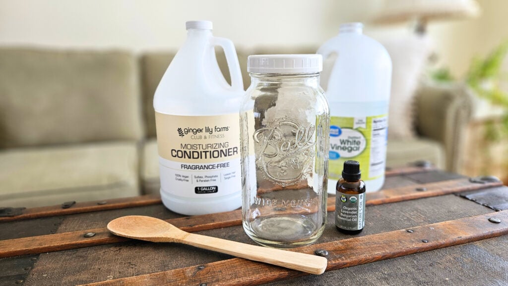 Quart size mason jar, gallon jug of distilled white vinegar, gallon jug of hair conditioner, 1 bottle of essential oil, and a wooden spoon.