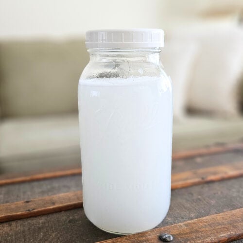 Half gallon mason jar of homemade liquid fabric softener sitting on top of a trunk.