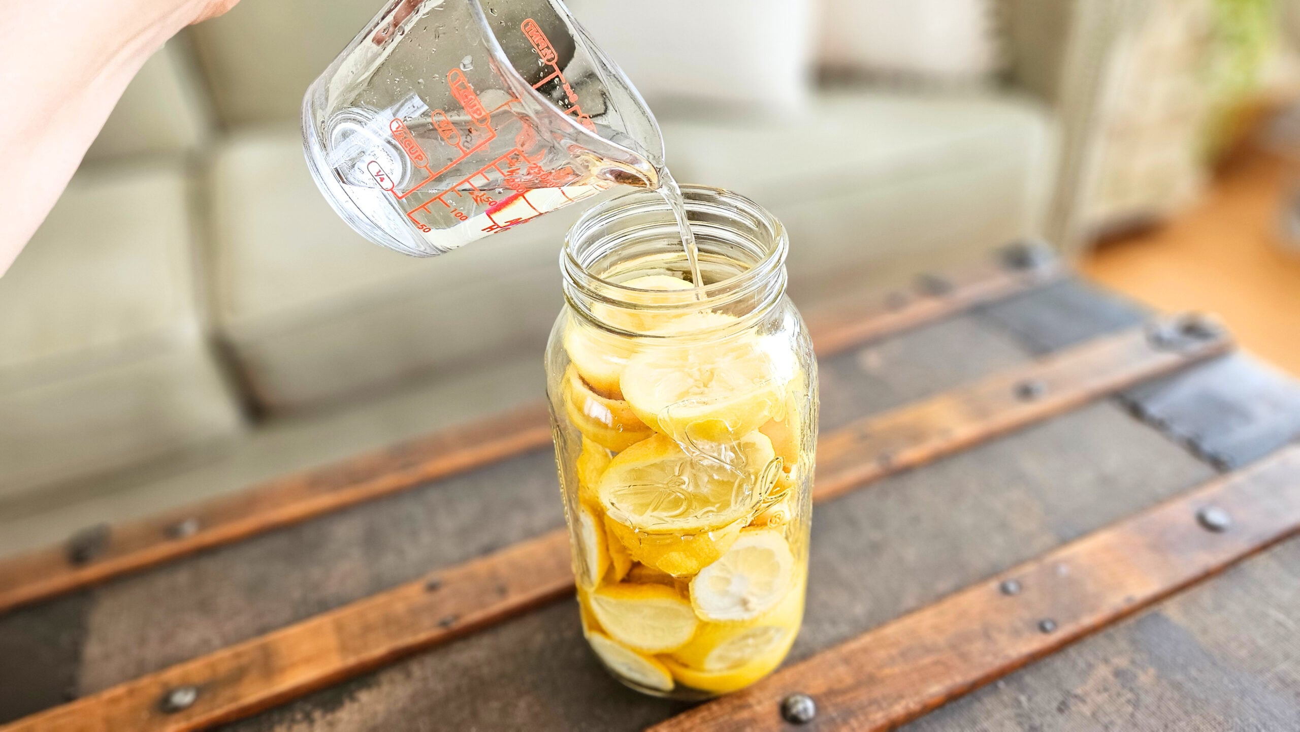 Pouring distilled white vinegar into a mason jar of lemon rinds.