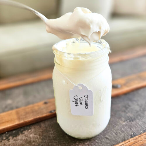 A spoonful of raw sour cream hovering over a pint jar.
