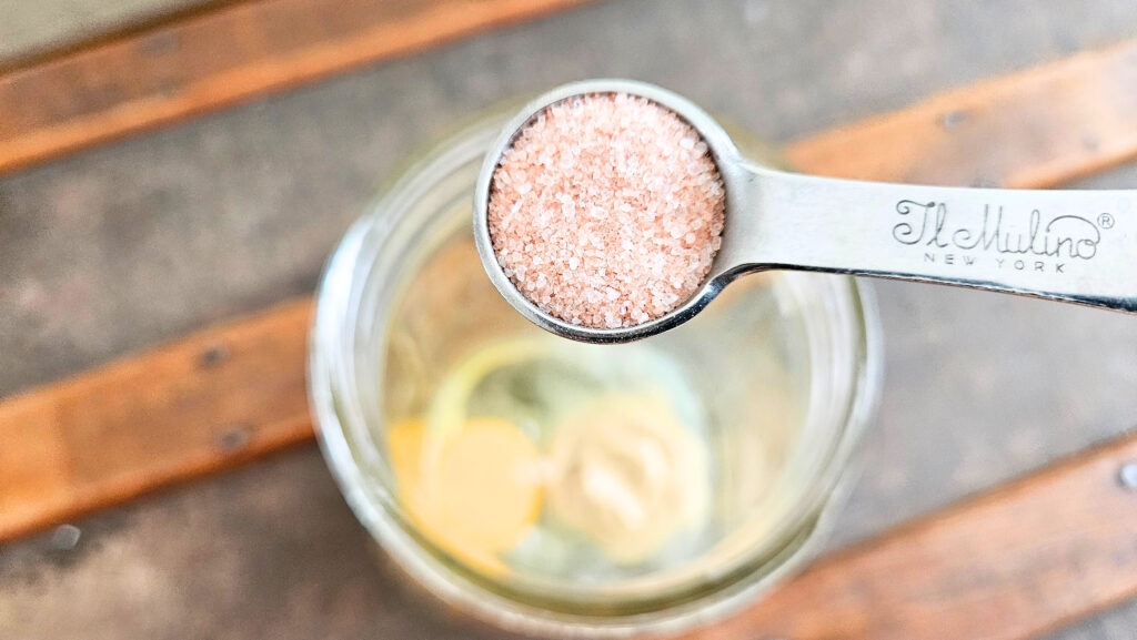 A measuring spoon of salt being added to a mason jar.
