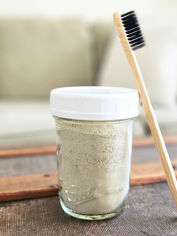 Half pint mason jar of homemade tooth brushing powder with a bamboo toothbrush.